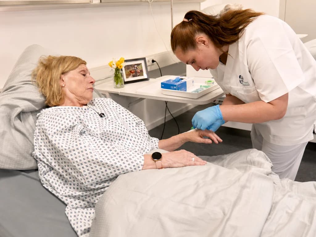 Lernende legt unter Aufsicht einen venösen Zugang am Unterarm einer Patientin im Skills Lab