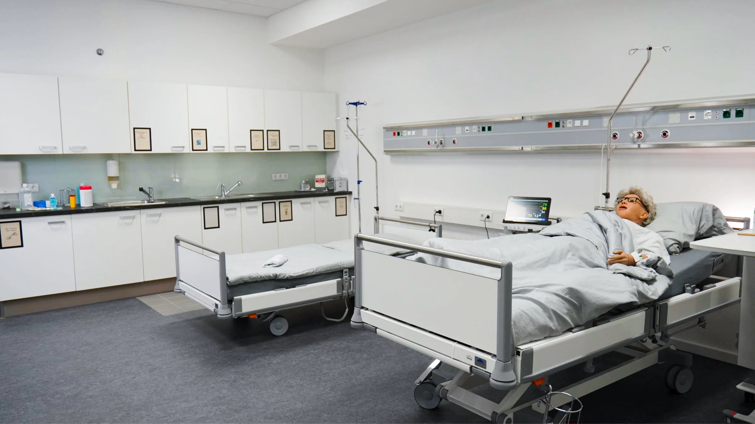 Skills Lab mit zwei Pflegebetten: Simulator unter der Decke, Vitalzeichen-Monitor und Infusionsständer